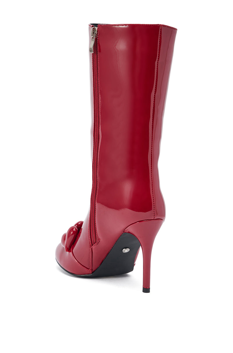 The AZALEA WANG FEDELE RED PATENT HEART EMBELLISHED BOOTIE features shiny red patent leather, a stiletto heel, side zipper, and heart accents near the toe. Shown from a side-rear angle on a white background for a glamorous look.