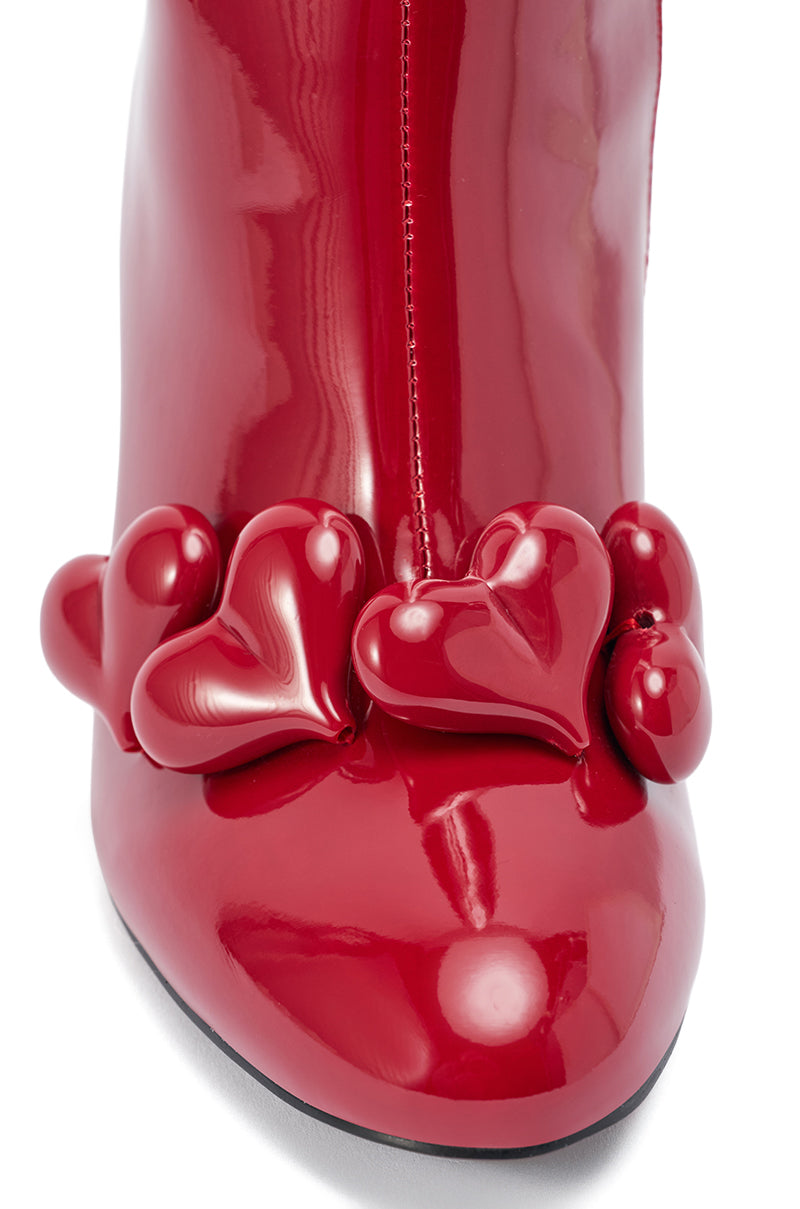 Close-up of the AZALEA WANG FEDELE Red Patent Heart Embellished Bootie, a shiny red stiletto with three glossy sculpted red hearts near the toe.