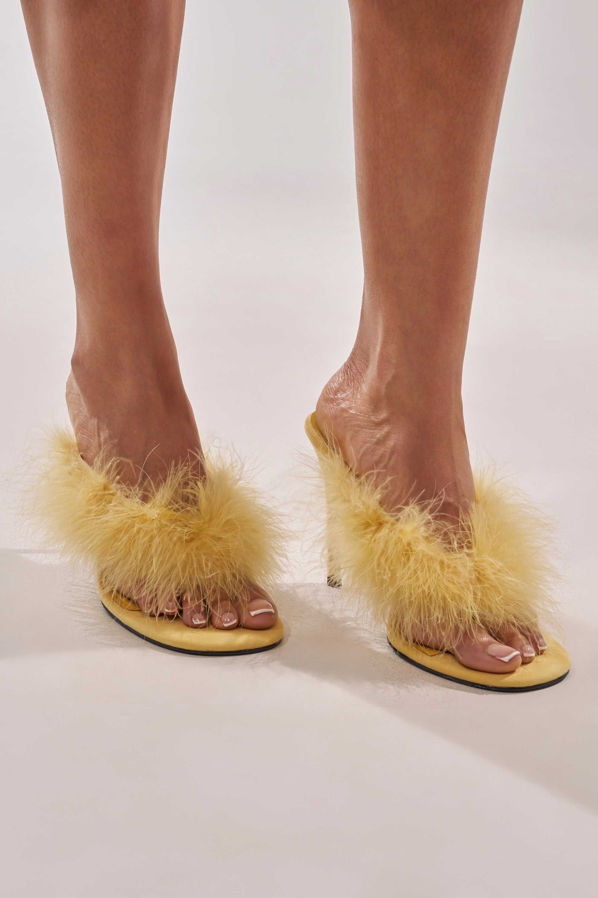 A person wears the AKIRA FEMINISTA Yellow Faux Suede Yellow Fur Embellished Kitten Heel Sandal with a comfort cushion insole, standing on a light surface. 1