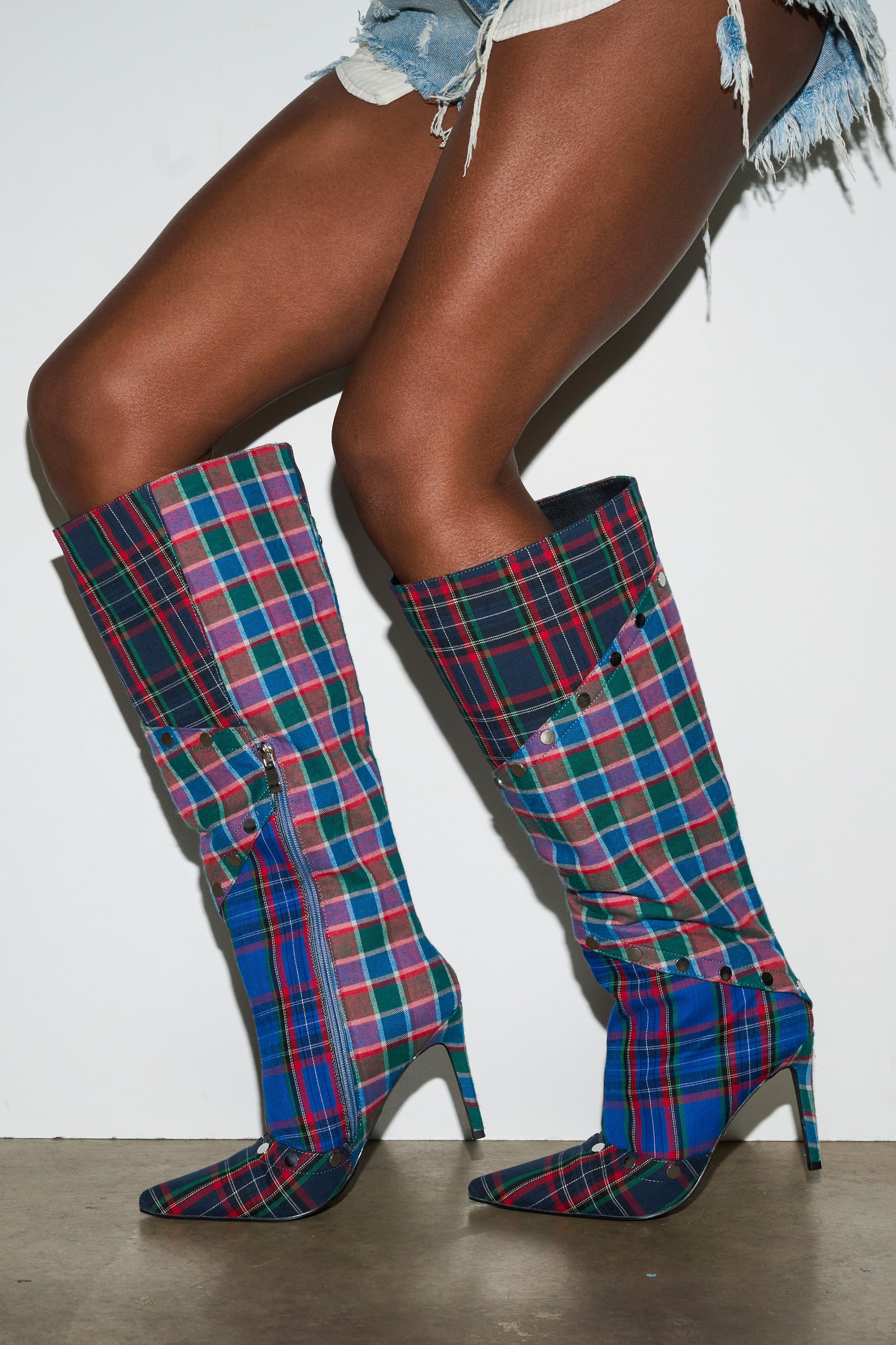A person stands against a plain white background, modeling frayed denim shorts and the AZALEA WANG FENMORE Plaid Multi Color Blocked Stiletto Boot. 1