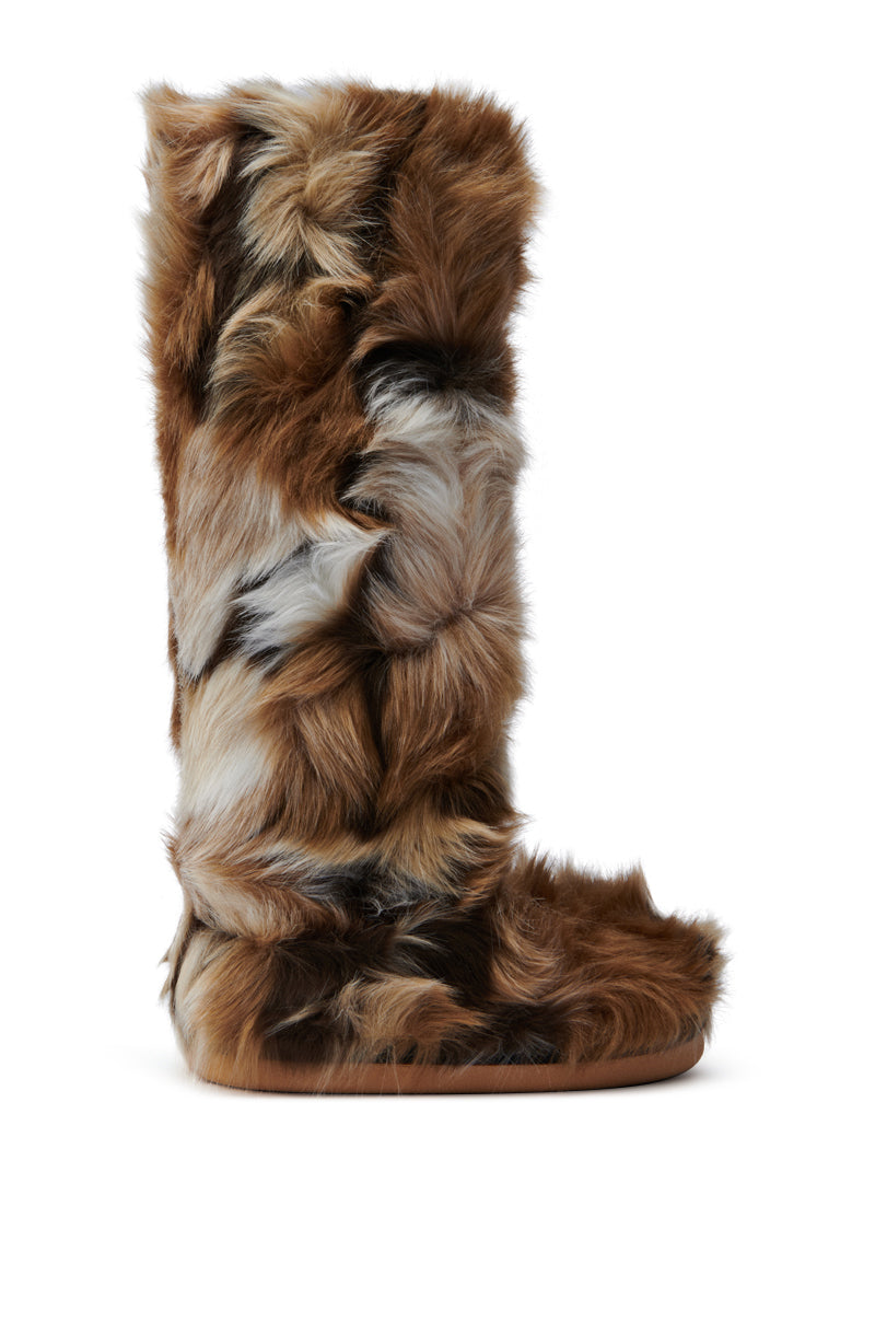 The AZALEA WANG FENNEC MULTI FUZZY FLAT KNEE HIGH BOOT is a tall, knee-high boot enveloped in thick, fluffy faux fur in shades of brown, grey, and white. The fur is patchy and uneven, providing the boot with a unique and wild appearance. Featuring a flat sole and no visible fastenings, this boot makes a bold statement.