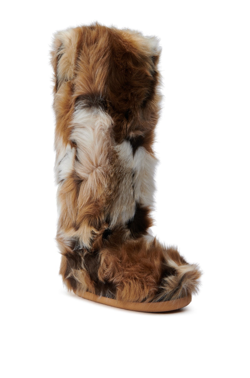 The AZALEA WANG FENNEC MULTI FUZZY FLAT KNEE HIGH BOOT is covered in a mix of brown, white, and black faux fur. It features a flat sole with a tan-colored base and has a fluffy, textured appearance that exudes coziness and warmth. The background is plain white.