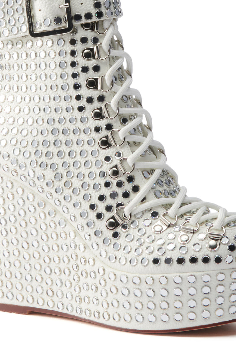 Close-up of the AZALEA WANG FERDY WHITE PLATFORM EMBELLISHED BOOTIE with a rhinestone-studded upper, white laces, silver buckle, wedge heel, textured surface, and angled brown sole for unique style.