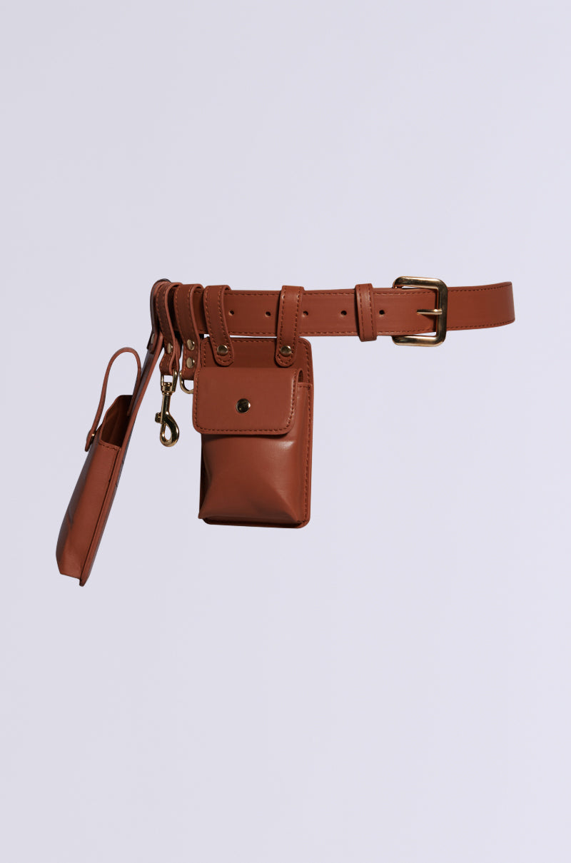 The UTILITY BELT is a brown faux leather accessory featuring several attached pouches and compartments, making it perfect as a utility belt. It includes a rectangular pouch, a small pocket with a flap, and a clip for attaching keys. The adjustable buckle ensures the perfect fit, all showcased against a plain white background.