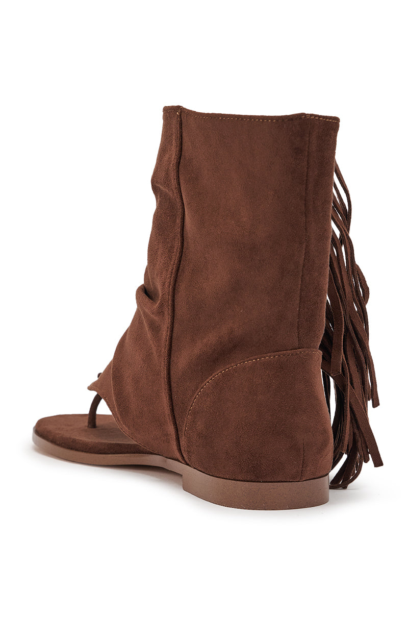 Side view of the AZALEA WANG FIDDA CHOCOLATE GLADIATOR FLAT SANDAL, an ankle-high brown faux suede sandal with a flat sole, closed heel, and decorative fringe detail on the back. 5