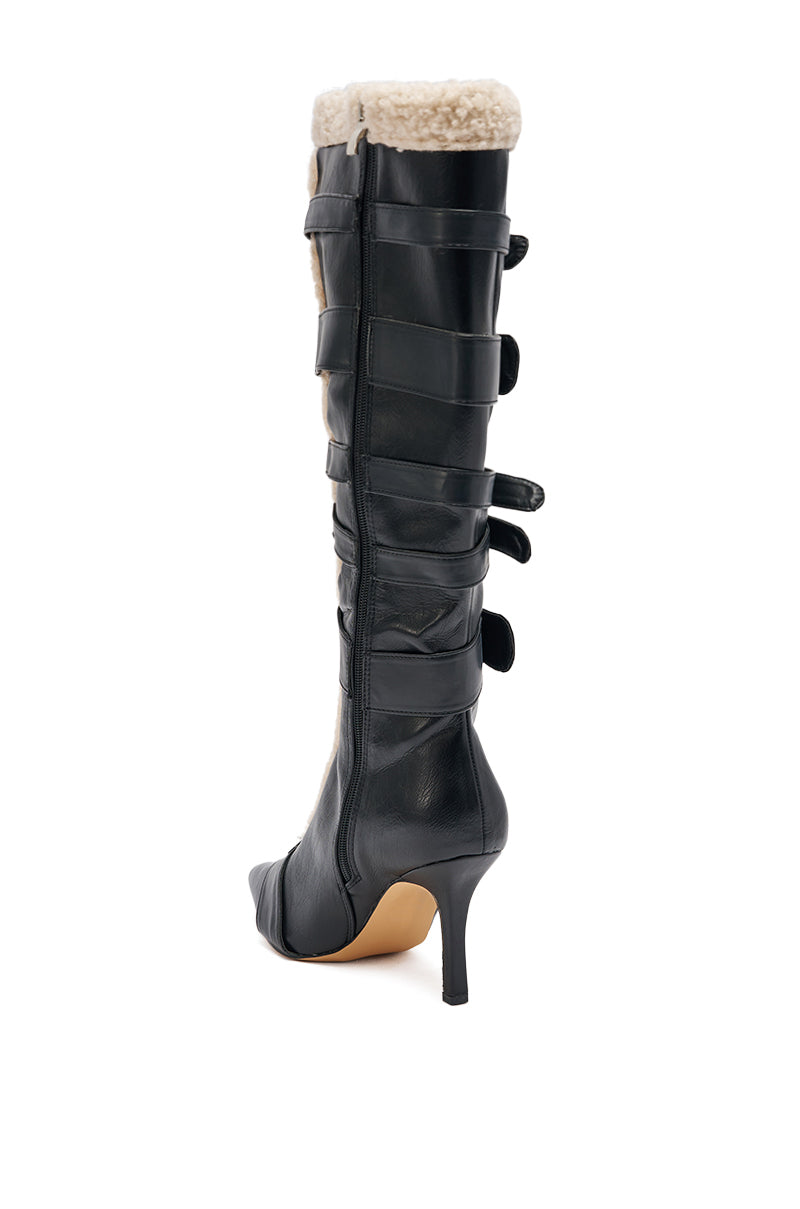 The AKIRA GOLD FIERO BLACK PU AND SHERPA BUCKLE is a black faux leather knee-high boot with pointed toe, high heel, side buckle straps, and sherpa trim at the top, shown on a white background.