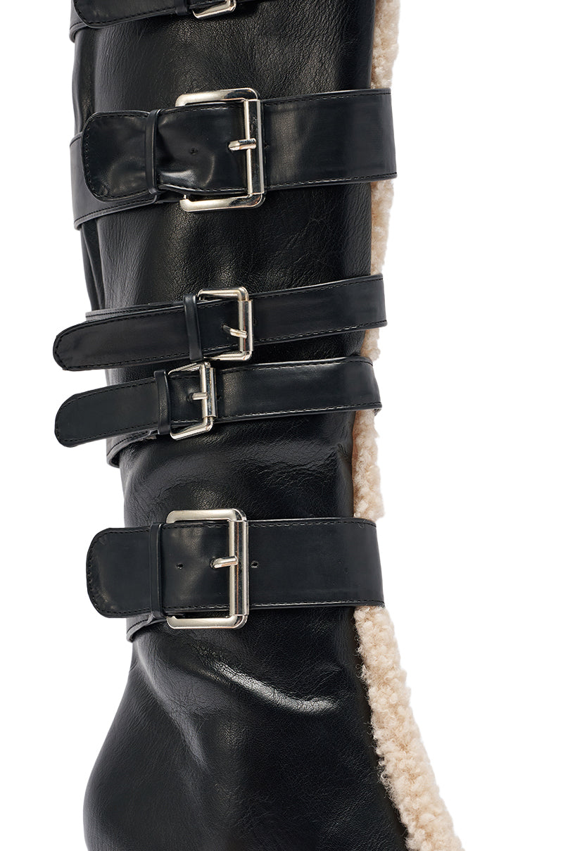 Close-up of the AKIRA GOLD FIERO BLACK PU AND SHERPA BUCKLE knee-high boot in black faux leather with four silver buckles and white sherpa trim along the side.