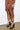 A person in a brown ribbed dress with leather sleeves stands against a white wall. The dress features a front zipper and a slit. They wear the AZALEA WANG FINLEA BROWN MULTI MATERIAL BOOTIE, adorned with high-heeled platform soles and lace-up detailing, finished with chic shearling trim.