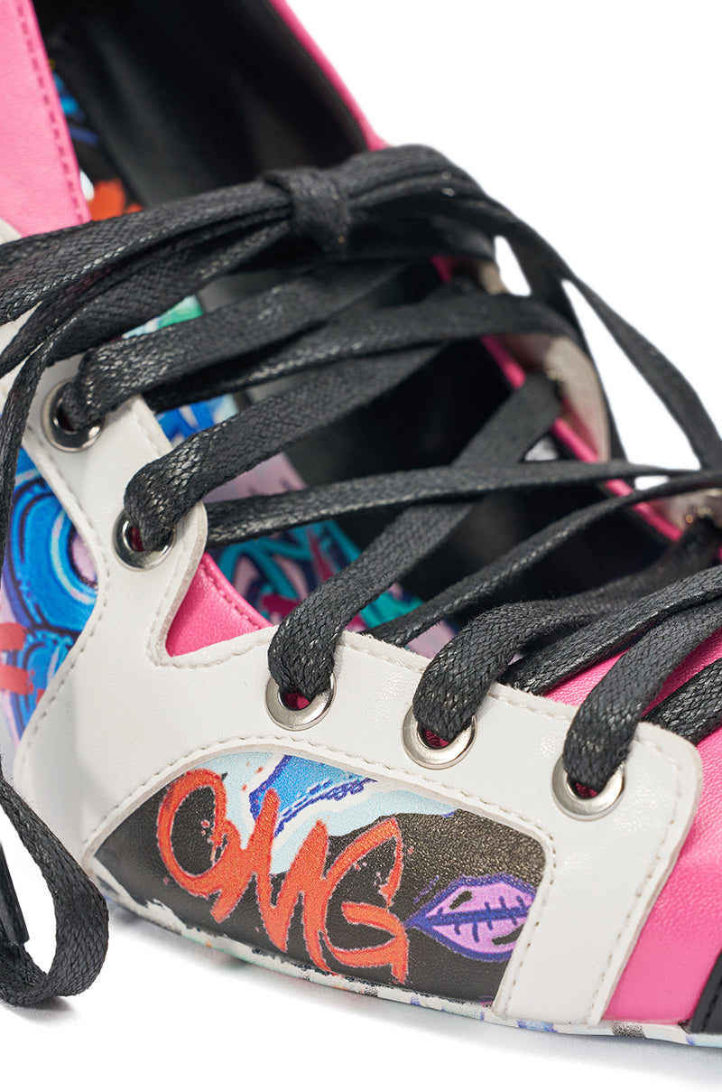 Close-up of the AKIRA GOLD FIRST STRING GRAFFITI PUMP, a lace-up stiletto with black laces, a white and pink upper, colorful graffiti-style designs, stylized text like "OMG," and a purple leaf. 8