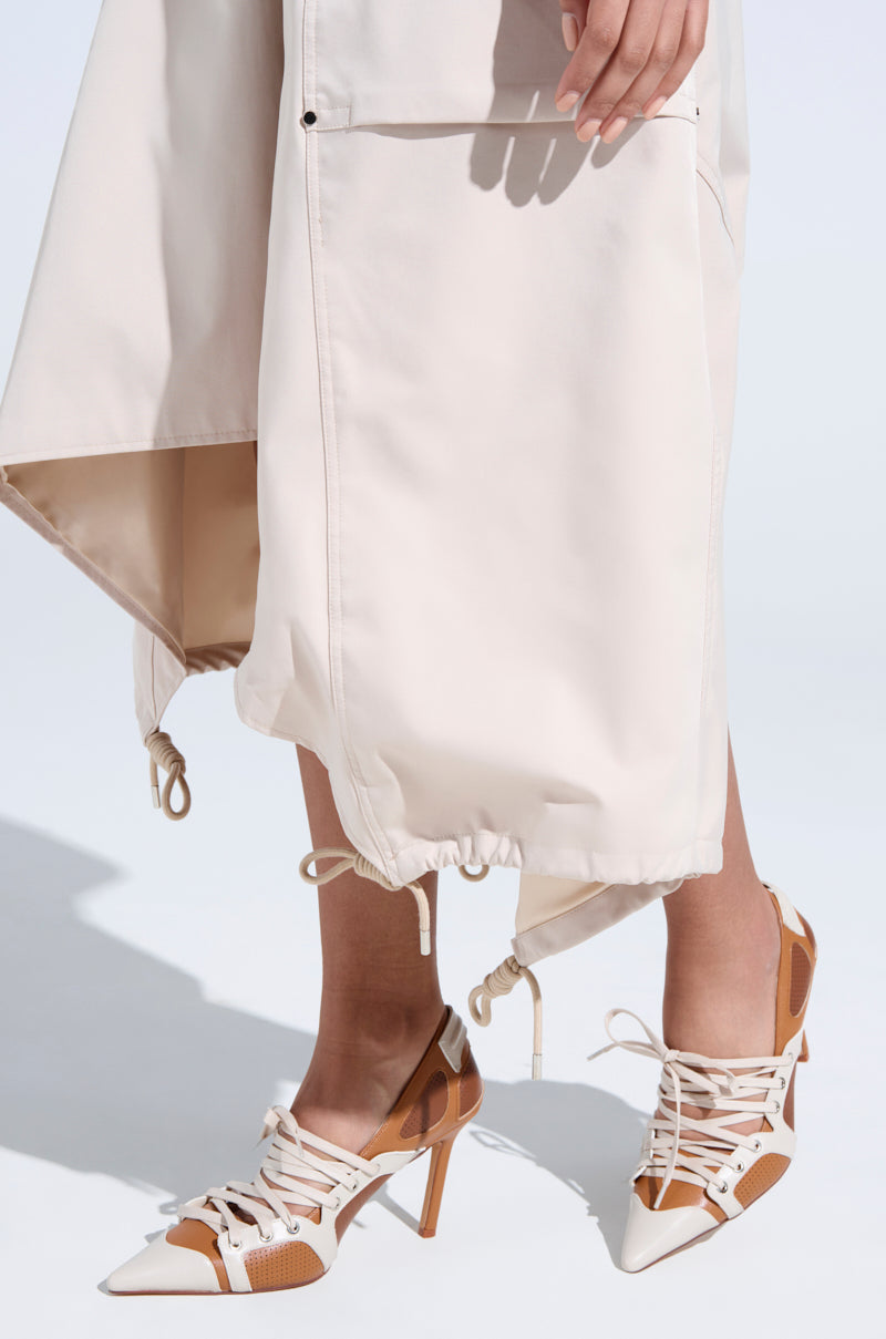A person wears a long beige skirt with drawstrings at the hem and AZALEA WANG FIRST STRING TAN COLOR BLOCK SPORTY PUMP—a stylish sneaker-style, lace-up high heel featuring brown and white perforated leather details against a bright backdrop.