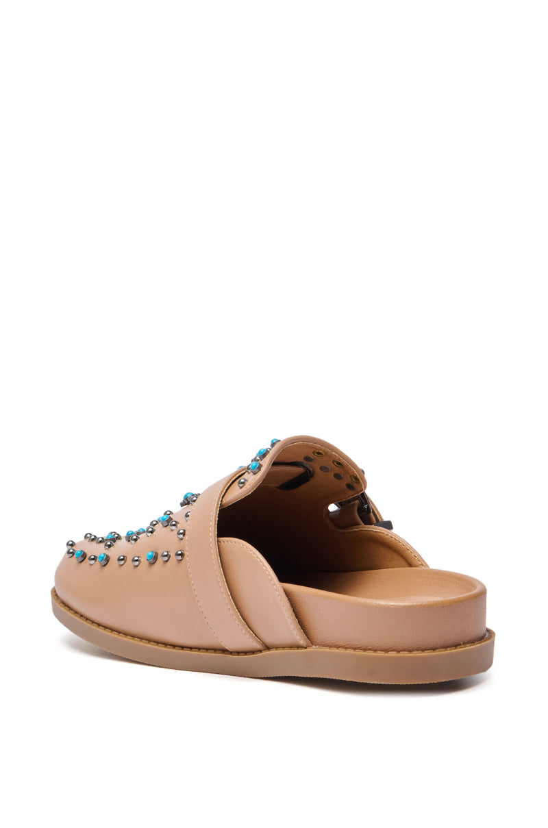 The AZALEA WANG FLAIR TAN EMBELLISHED CLOG is a beige faux leather slip-on with a low sole, blue and silver studs on the upper, and western-style mule vibes. Pictured from an angle showing the back and inner side.