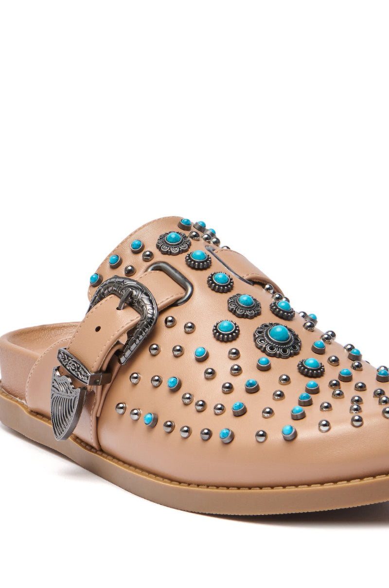 The AZALEA WANG FLAIR TAN EMBELLISHED CLOG is a tan faux leather slip-on mule with silver studs, turquoise stone accents, a western buckle, flat sole, and bold western-inspired details for an eye-catching look.