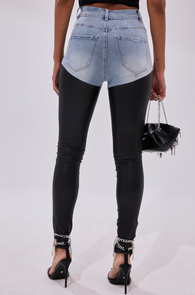 A person stands with their back to the camera, wearing FLEX FIT EXTREME STRETCH HIGH WAIST SKINNY JEANS WITH FAUX LEATHER, styled with black high heels, chain anklets, and a small black handbag.