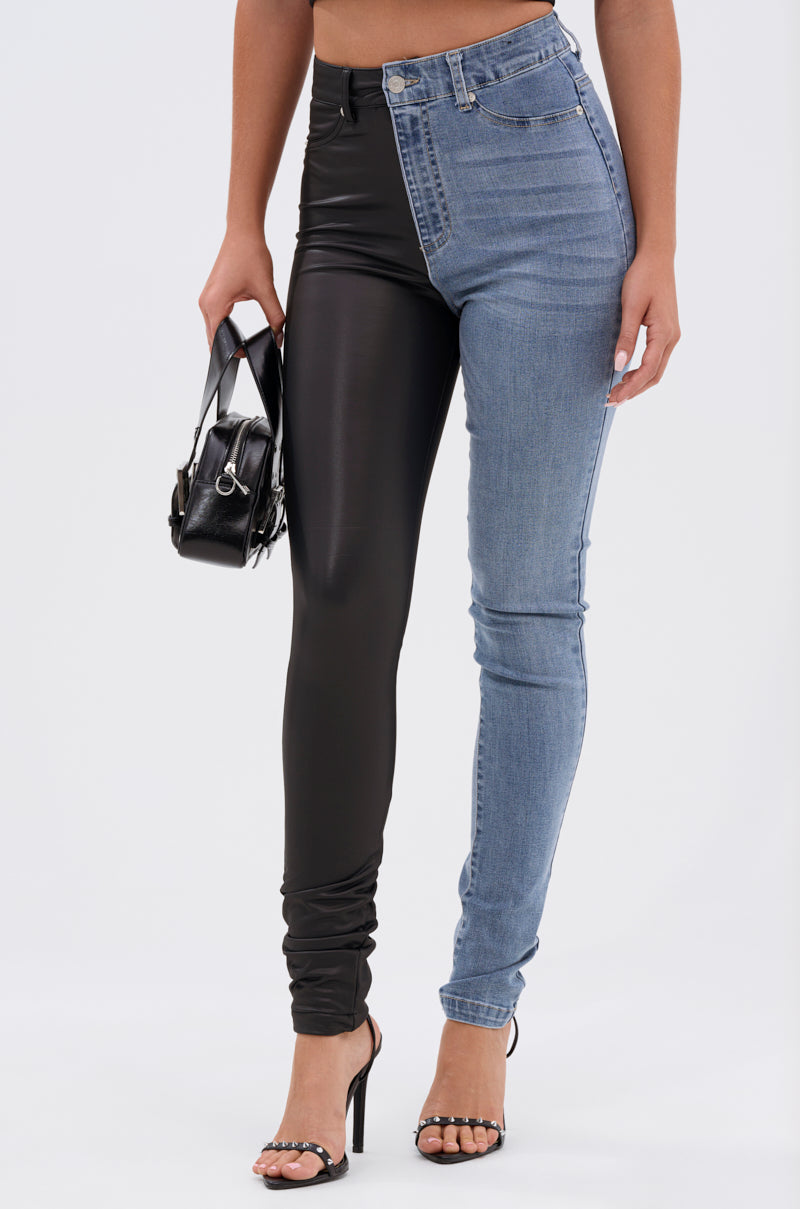A woman poses against a white background in FLEX FIT EXTREME STRETCH HALF AND HALF PU HIGH WAIST SKINNY JEAN—one leg in black faux leather, the other in stretch denim—paired with high-heeled sandals and a small black handbag.