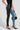 The individual is dressed in Flex Fit Extreme Stretch Half and Half PU High Waist Skinny Jeans, featuring one leg in sleek black leather and the other in blue denim. They complement this striking look with black polka dot heels while carrying a small black handbag, all set against a minimalist white background that highlights their bold high-fashion style.