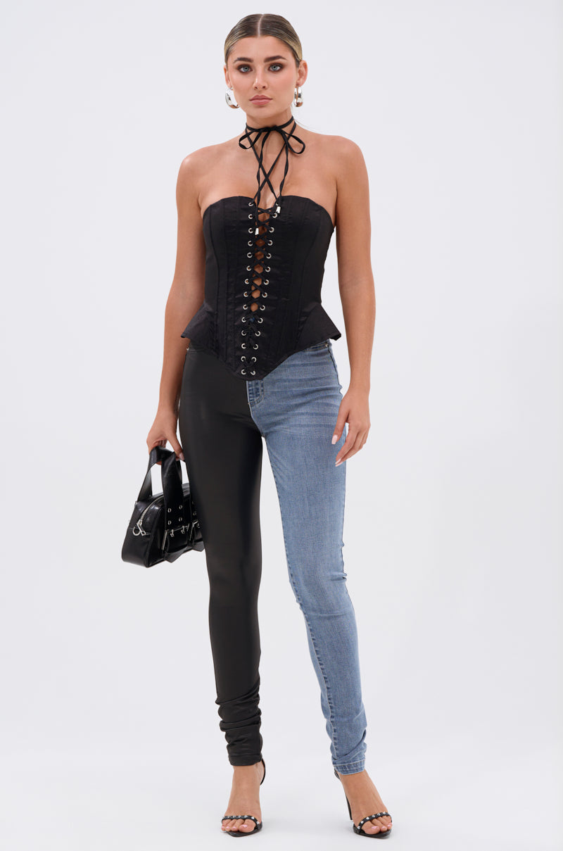 A woman stands against a white background wearing the FLEX FIT EXTREME STRETCH HALF AND HALF PU HIGH WAIST SKINNY JEAN with a black corset top, hoop earrings, black handbag, and black high-heeled sandals.