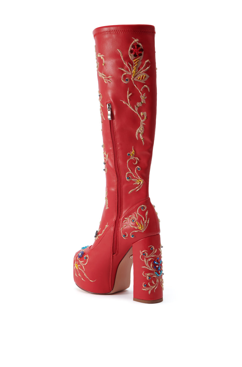 The AZALEA WANG FLIPPER RED PU WITH EMBELLISHMENTS CHUNKY BOOT is a red knee-high boot made from faux leather, featuring a platform heel and intricate floral embroidery in various colors. It also includes a side zipper, a chunky heel, and detailed stitching on an immaculate white background.