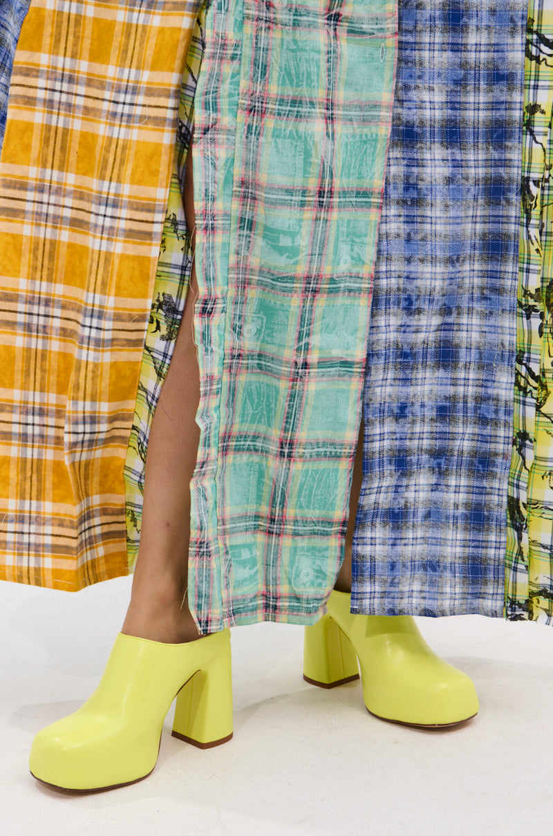 A person shows bare legs and bright yellow AZALEA WANG FLOREA LIME CLOG STYLE PUMPS while wearing a long patchwork plaid skirt in yellow, teal, and blue on a white floor.