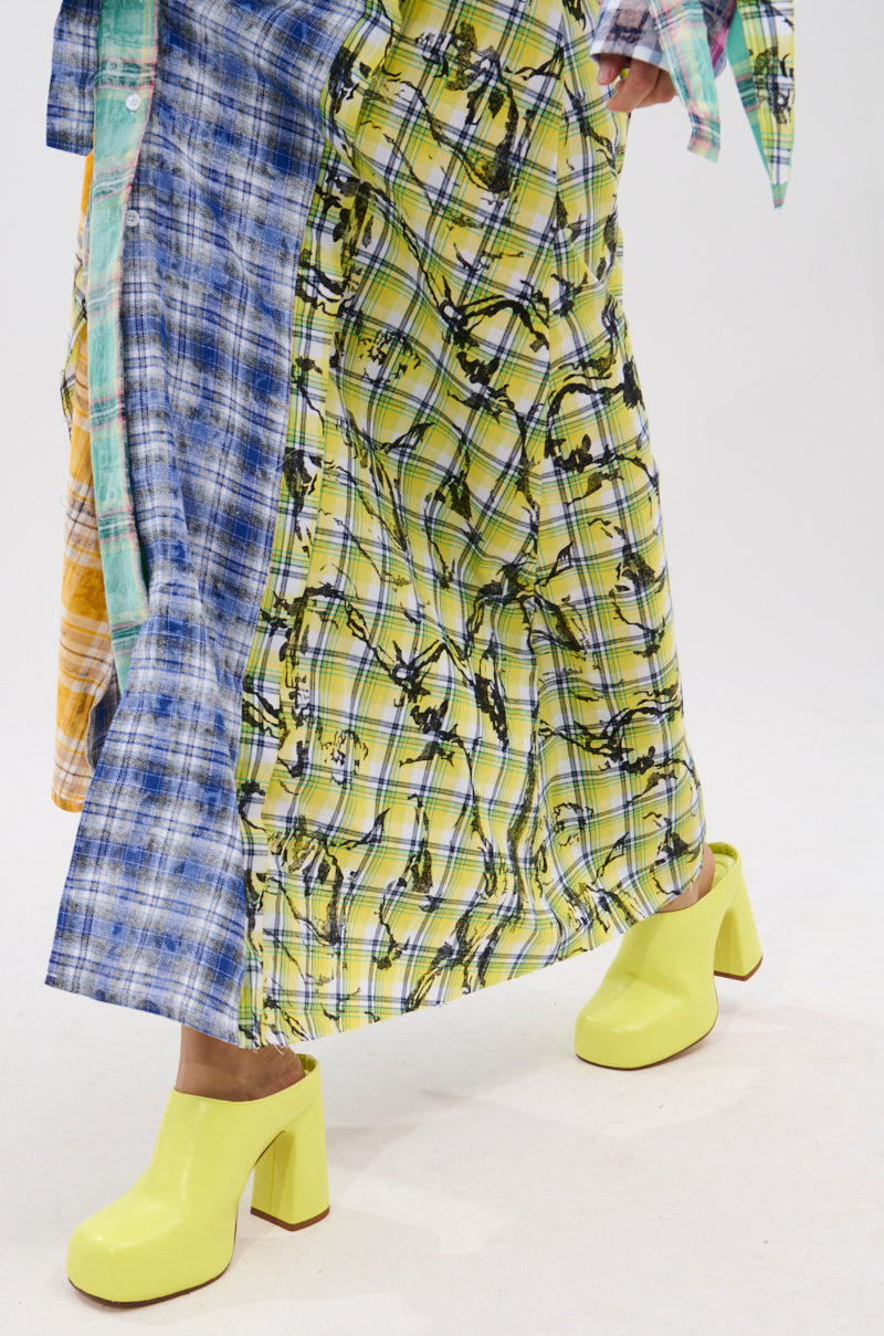 A person wearing a long, colorful plaid skirt with blue and yellow patterns pairs it with the AZALEA WANG FLOREA LIME CLOG STYLE PUMP while walking on a white surface.