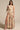 A woman wears the JOAN BLOUSE, a yellow floral print asymmetrical one-shoulder crop top, paired with a matching maxi skirt with a high slit. She exudes confidence in pink strappy heels against a neutral background.