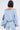 A person with a short bob is seen from behind wearing the FLORAL LIFE OFF THE SHOULDER BLOUSE, featuring voluminous sleeves and a blue-and-white floral print—paired with matching trousers for a chic spring look.
