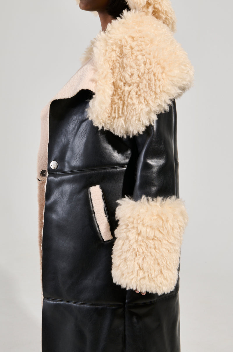 A person wearing the SHE GOT IT FLUFFY PU TRENCH WITH BONDED SHERPA, showcasing a chic black leather design complemented by a plush Sherpa faux leather lining on the hood, cuffs, and collar. The side view accentuates the elegant contrast between the sleek leather and fluffy Sherpa textures.
