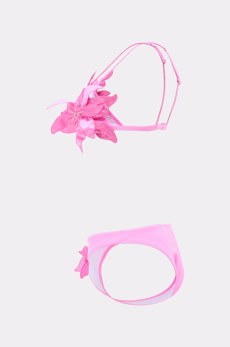 The IN BLOOM SWIMSUIT is shown on a light background, featuring a pink floral appliqué top with petal details and matching high-leg bikini bottoms with a flower accent on one side.