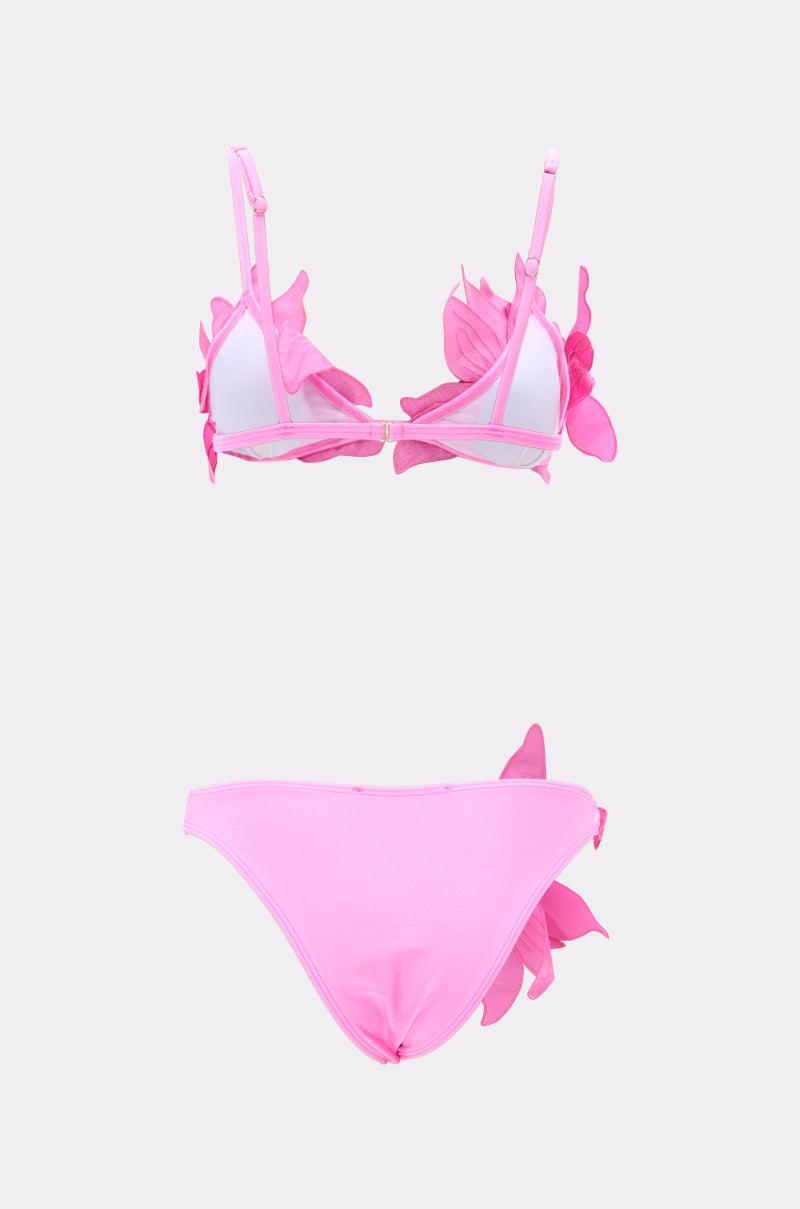 The IN BLOOM SWIMSUIT is a two-piece pink bikini with 3D floral appliqués on the top and one side of the high-leg bottoms, shown against a plain white background.