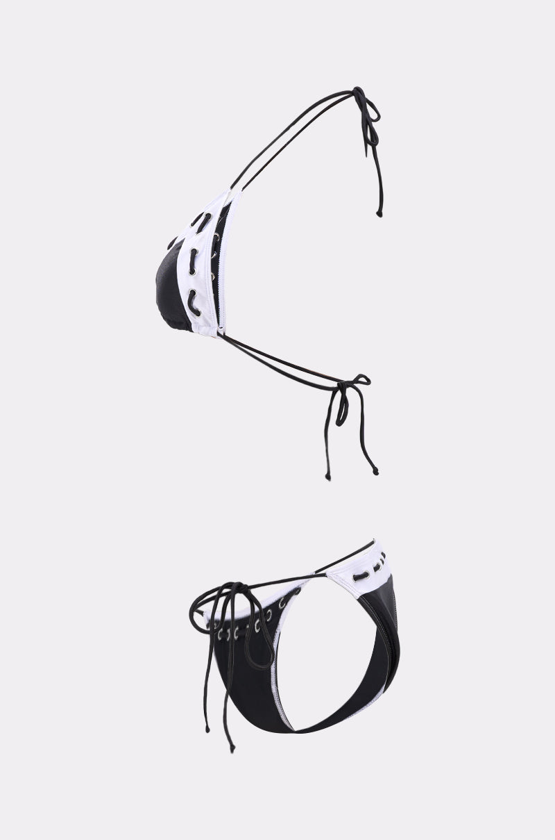 The SPORTY VIBES SWIMSUIT is a black and white set with a string bikini silhouette and lace-up details on both the top and bottoms, shown against a plain light gray background. 1