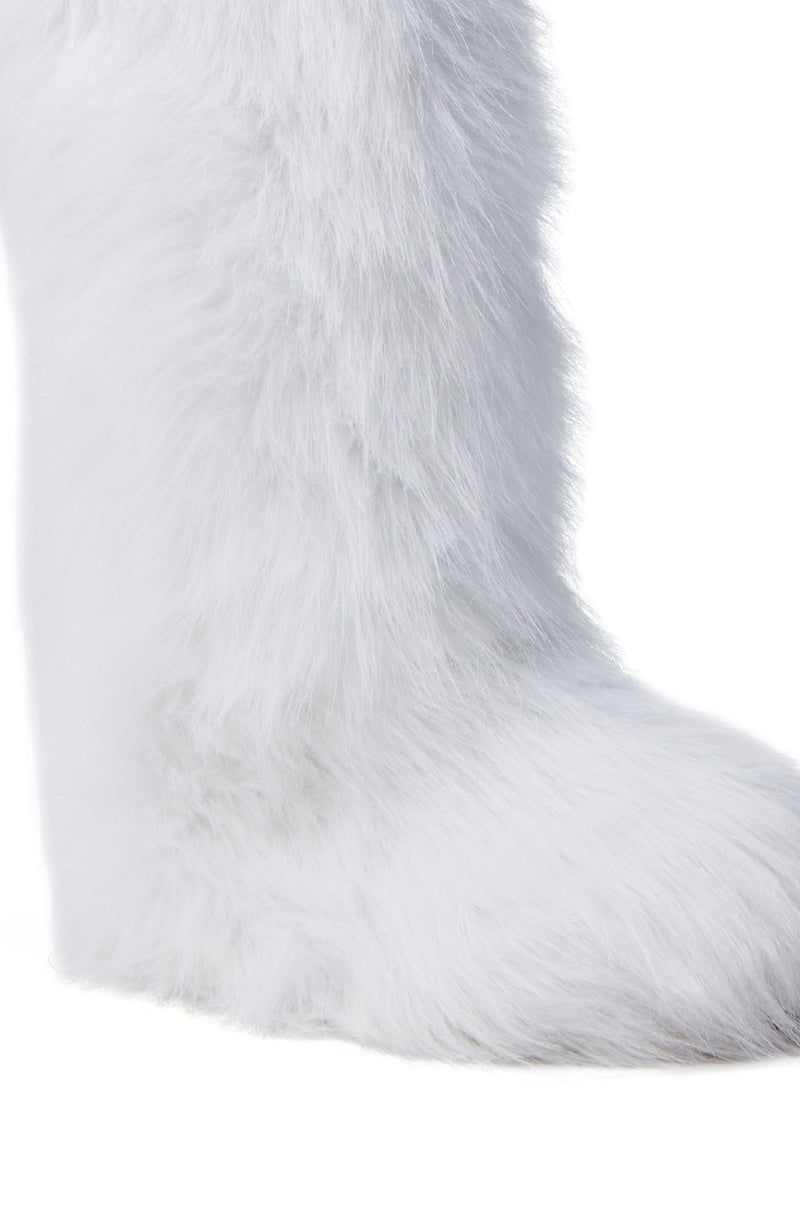 The FONDA WHITE FLAT BOOT, designed for winter, is showcased in a close-up. It features a mid-calf design enveloped in soft white faux fur, exuding warmth and coziness. The boot’s lower half stands out against a plain white background.