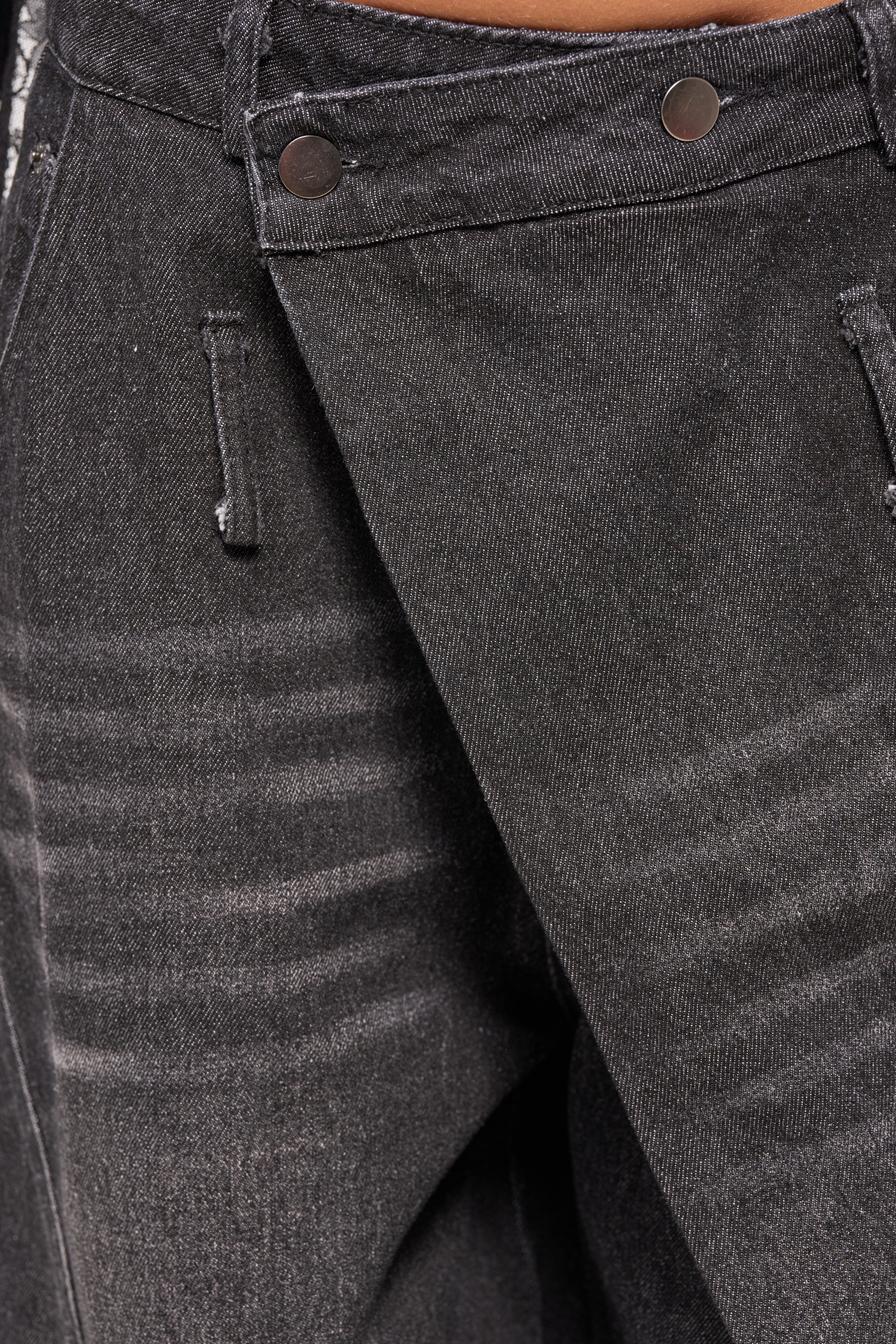 Close-up of the IZZY RELAXED DENIM IN BLACK WASH featuring a barrel silhouette, diagonal flap detail, two metallic buttons at the waistband, visible faded lines, and contrast stitching for a wide-leg look. 7