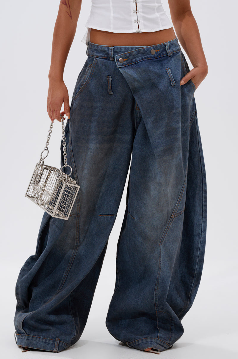 A person wearing IZZY RELAXED DENIM high-rise, wide-leg dark blue jeans and a white top holds a small metallic cage handbag with a chain strap against a plain background.