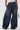 A person is shown from the back wearing the IZZY RELAXED DENIM jeans with large cuffs and pockets, paired with a white lace-up top and holding a silver geometric handbag.