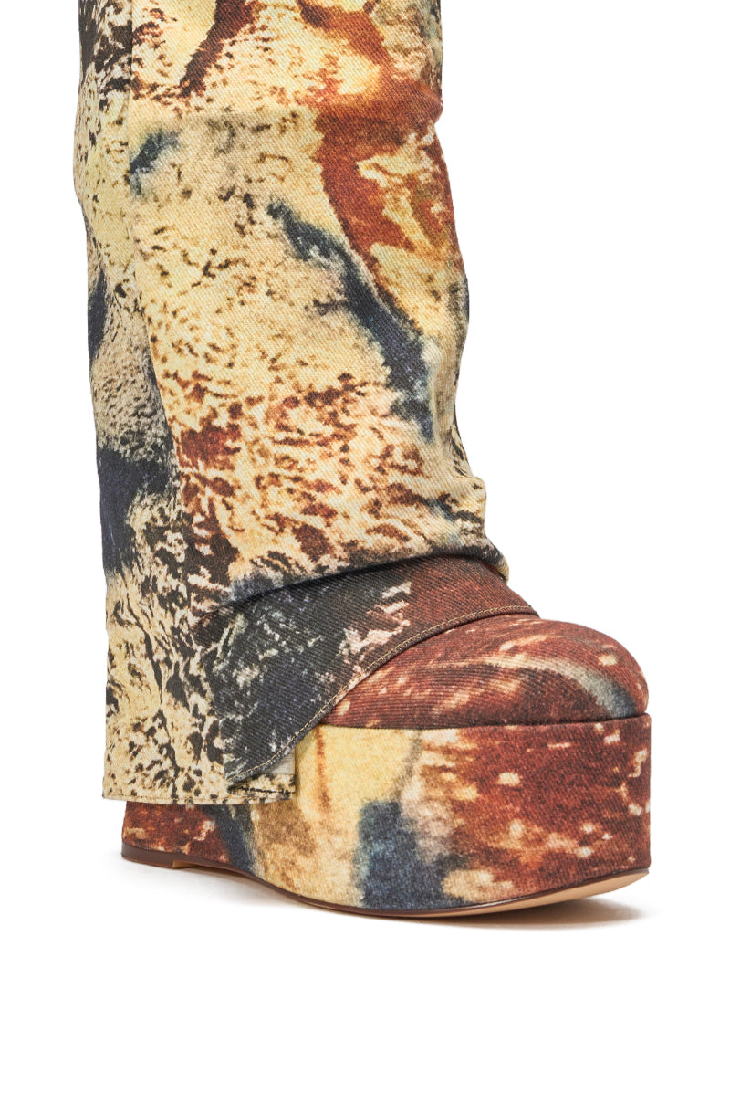 A close-up of the AZALEA WANG FRANKEYE MULTI MATERIAL FLATFORM BOOT, featuring multicolored, textured fabric with earth-toned abstract patterns, partially obscured by matching fabric pants. 5