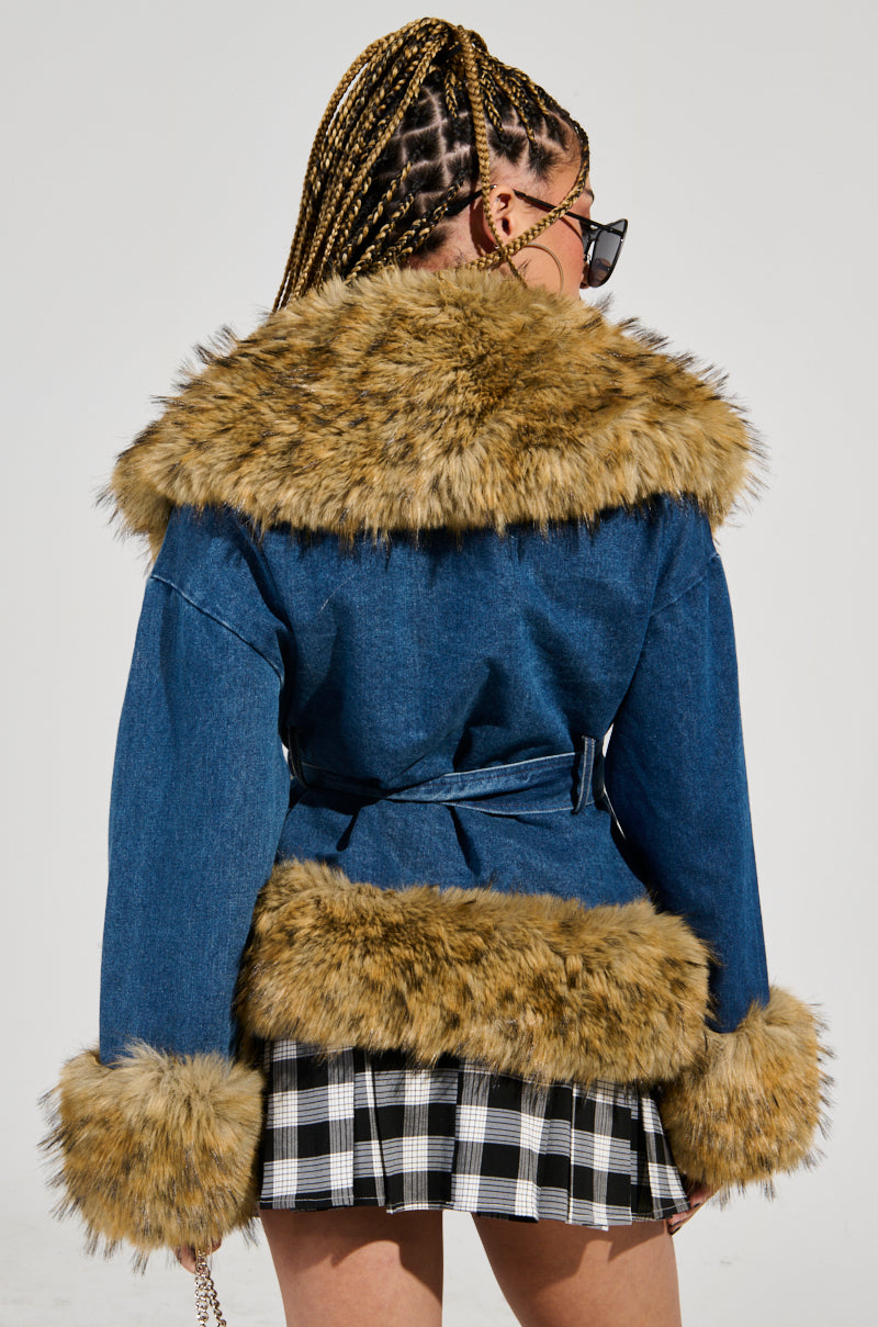 A person with braided hair, wearing sunglasses, is seen from behind. They sport the FREDDIE FUR TRIM DENIM MOTO jacket, featuring faux fur trim on the collar, cuffs, and hem, perfectly paired with a black and white plaid skirt.