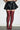 A person wears a black quilted mini skirt and AZALEA WANG FREJYA BURGUNDY LEOPARD LACE THIGH HIGH BOOTS, standing against a white wall. Only the lower half of the body is visible.