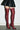 A person in a black textured mini skirt and AZALEA WANG FREJYA Burgundy Leopard Lace Thigh High Boots with stiletto heels stands against a plain white wall on a concrete floor.