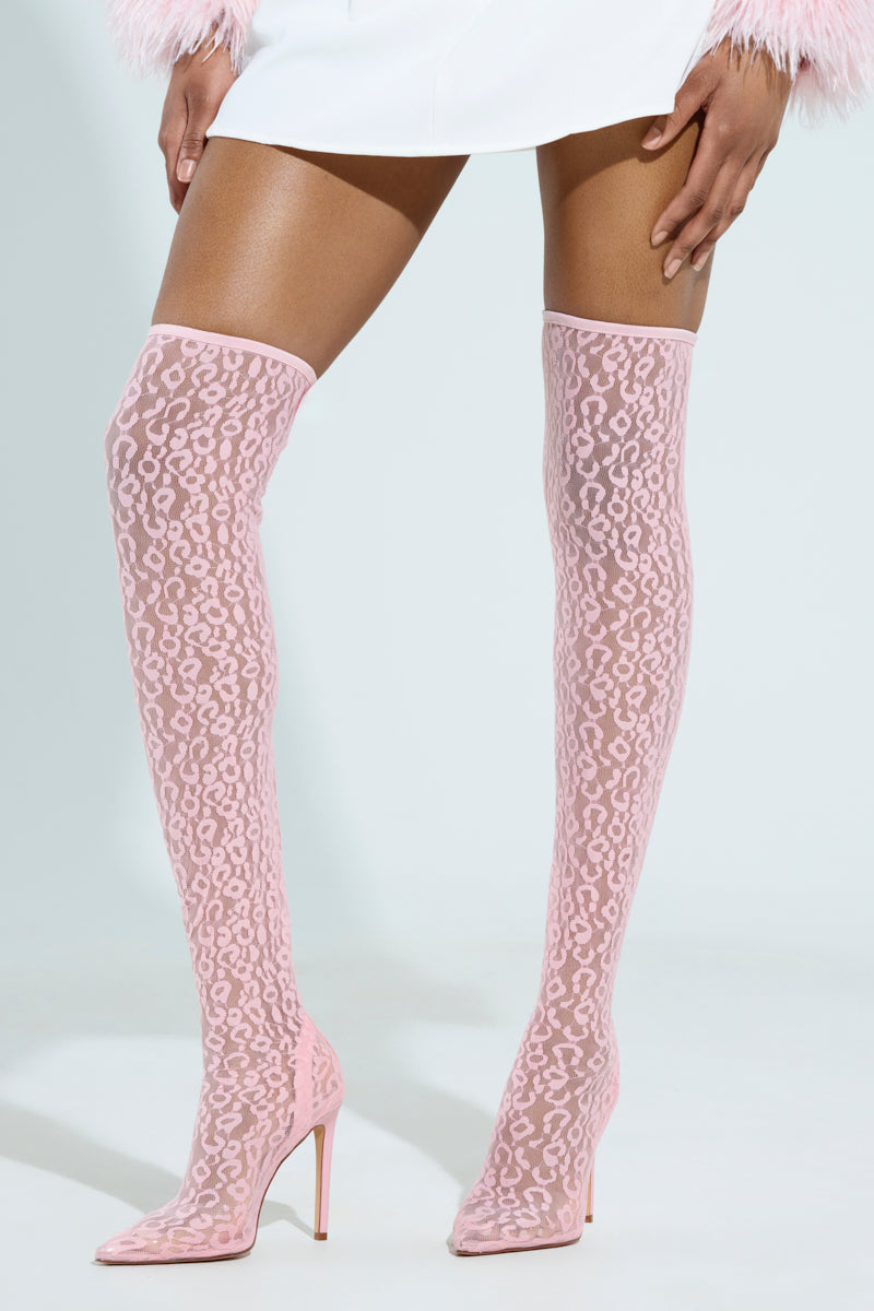 A person wearing AZALEA WANG FREYJA over-the-knee pink lace boots with stiletto heels and a white feather-hem skirt against a plain white background.