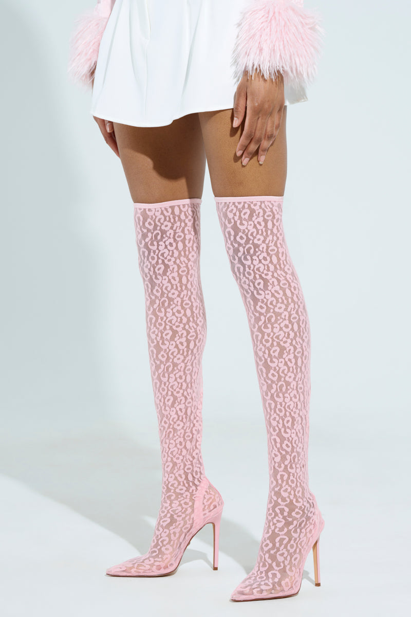 Someone is strutting in pink Azalea Wang Freyja over-the-knee lace boots, featuring a leopard print design and stiletto heels. They're also wearing a white outfit with vibrant pink feathered cuffs, completing the bold ensemble.