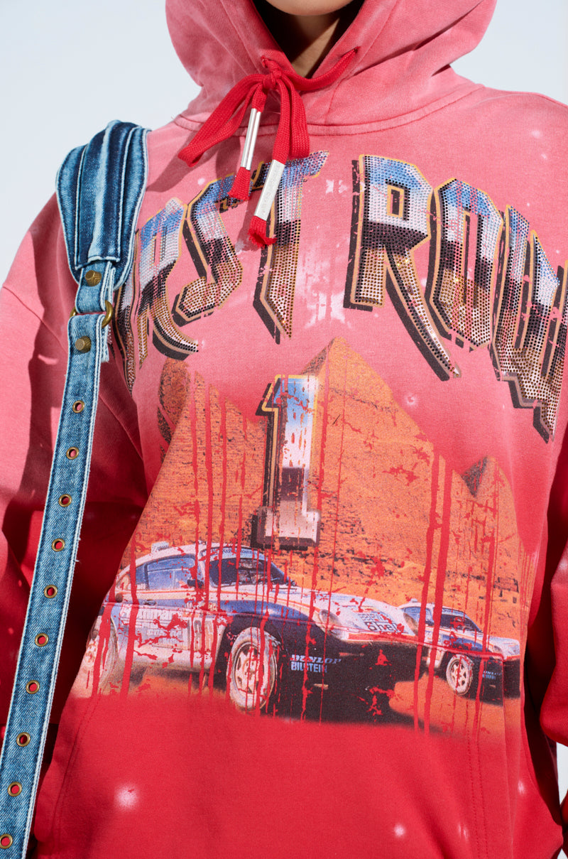 The person wears an ombre red-washed "IN THE FAST LANE HOODED SWEATSHIRT" featuring "FIRST ROW 1" and car racing graphics, complemented by a matching red drawstring and a denim strap over their shoulder.