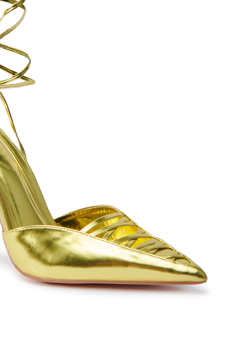 The AZALEA WANG FRIDLI YELLOW LACE UP PUMP showcases a glossy golden finish, featuring a stiletto heel and pointed toe. Crisscross straps provide an elegant touch, wrapping around the ankle above the heel, all set against a white background.