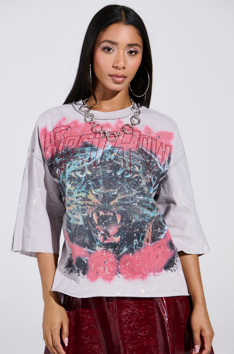 A woman with long hair wears the PRIMAL FURY CROPPED GRAPHIC SWEATSHIRT, featuring a vintage jaguar design with red splashes. She pairs it with large hoop earrings and a chunky chain necklace, standing confidently against a white background with her hands by her sides.