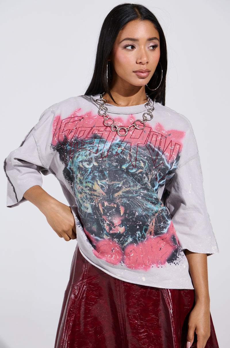 With vintage-inspired style, a person with long black hair and hoop earrings wears the PRIMAL FURY CROPPED GRAPHIC SWEATSHIRT, featuring a roaring panther graphic with red and blue accents, paired with a shiny red skirt and a chunky silver chain necklace.