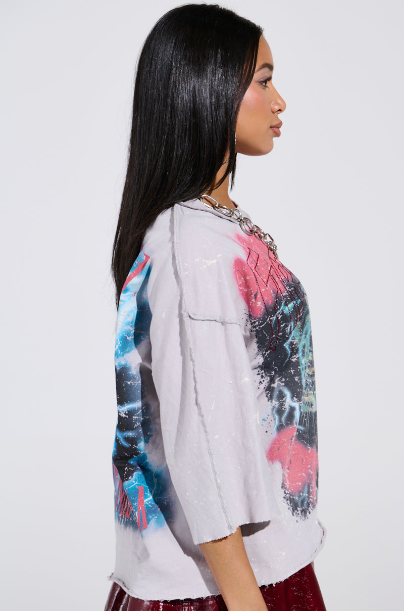 A person with long black hair is wearing a light gray PRIMAL FURY CROPPED GRAPHIC SWEATSHIRT featuring colorful designs. They are turned to the side, showcasing a layered necklace and the sweatshirt's loose fit. The plain white background highlights their stylish ensemble.