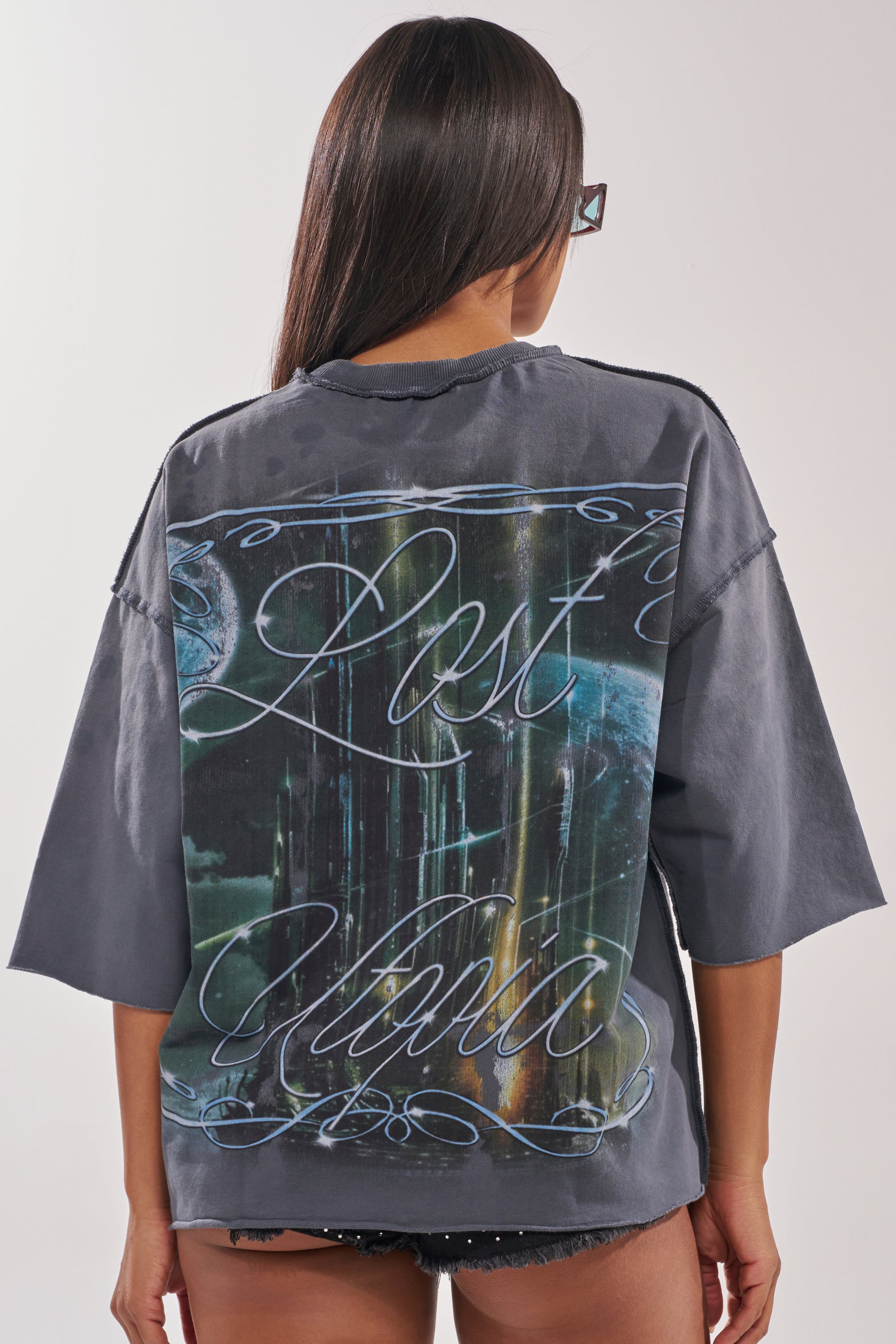 Woman with long dark hair wears sunglasses and a gray oversized FIRST ROW DIVINE RIGHT FRENCH TERRY TEE, featuring “Lost Mind” on the back, creating an effortless street style vibe against a plain background. 3
