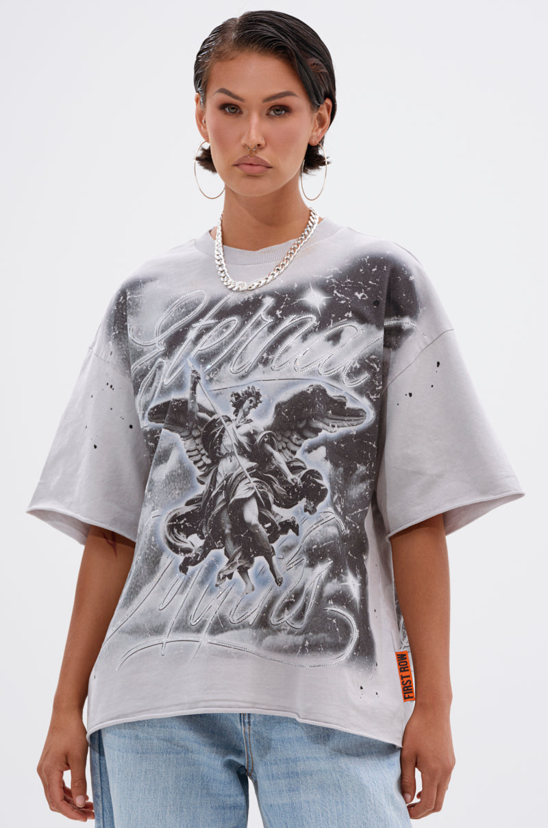 Wearing the BOUNCE BACK OVERSIZED TEE, a light gray grunge graphic t-shirt with an angel and cursive design, paired with light blue jeans and a chain necklace against a white background.