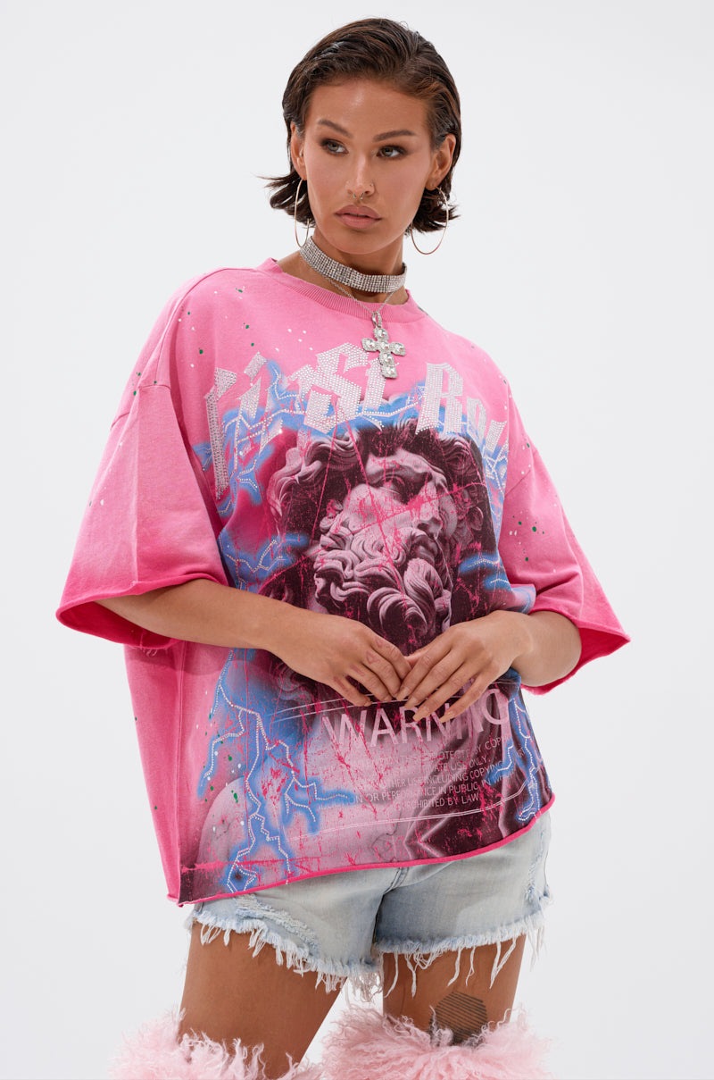 A woman poses confidently in the FADE INTO BLACK OVERSIZED TEE featuring statue and lightning graphics, paired with denim cut-off shorts, a chunky cross necklace, and pink furry boots against a plain white background.