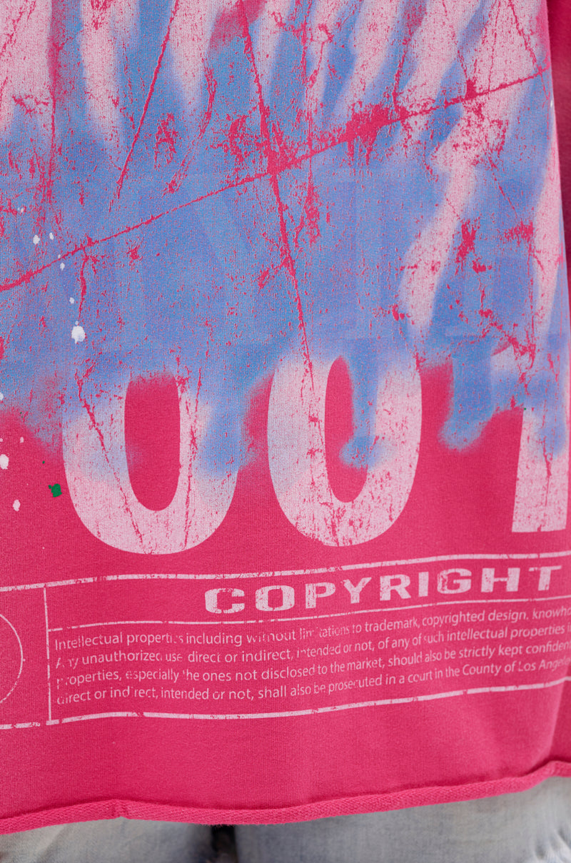 A close-up of the FADE INTO BLACK OVERSIZED TEE, a pink graphic t-shirt with blue and white paint splatters, "COPYRIGHT" text on the front, and faint legal terms printed in white along the bottom edge.