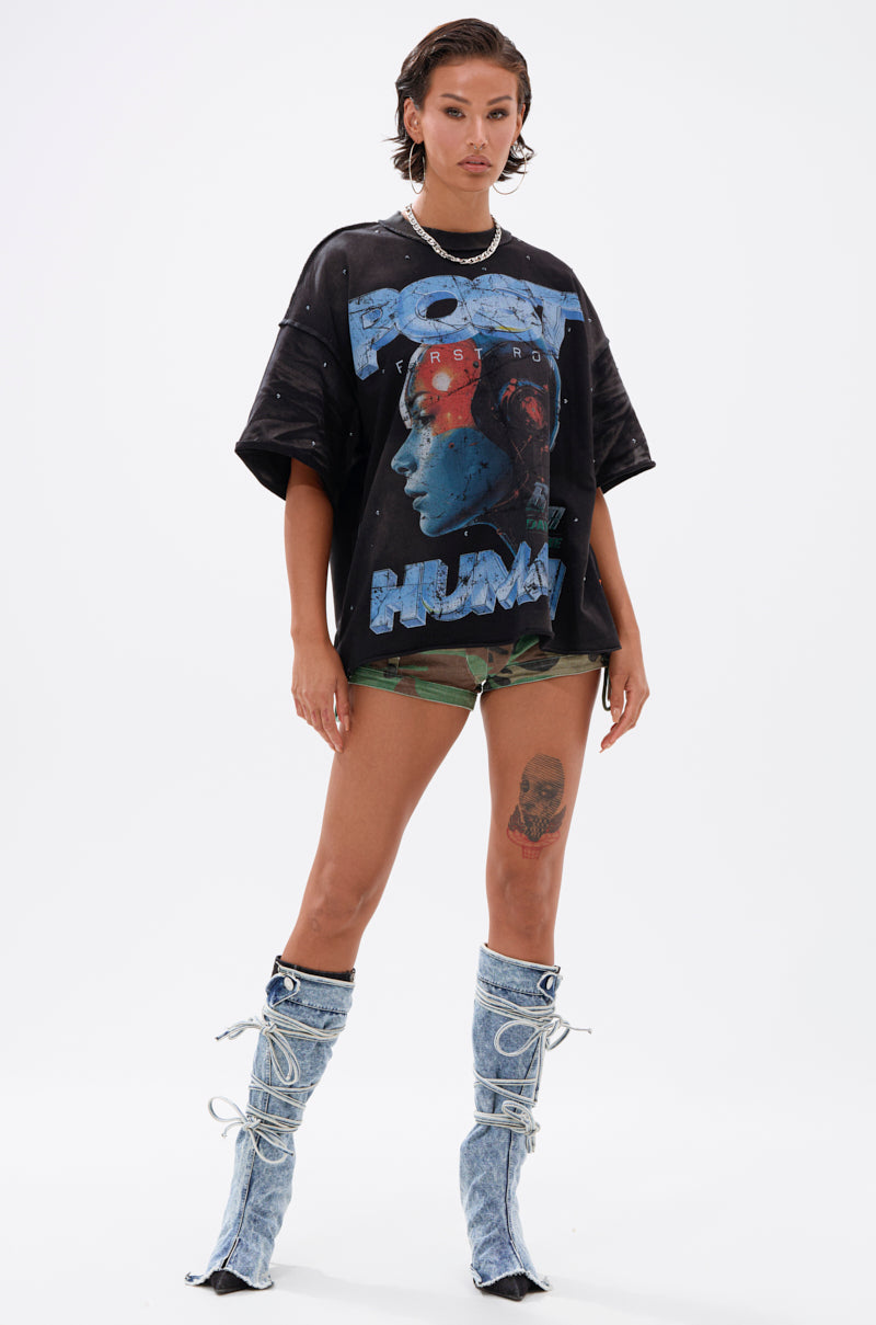 A woman stands confidently in THE FUTURES CALLING FRENCH TERRY GRAPHIC TEE, camo skull-print shorts, and knee-high light blue lace-up boots against a plain white background.