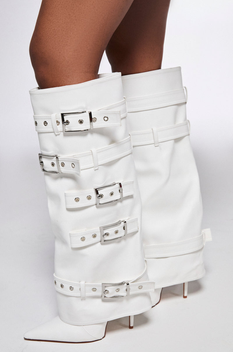 The AZALEA WANG FROST WHITE BELTED STILETTO BOOT is a knee-high, vegan leather boot with pointed toes. Featuring multiple silver buckles and straps, these boots have a bold, edgy design that stands out against a white background.